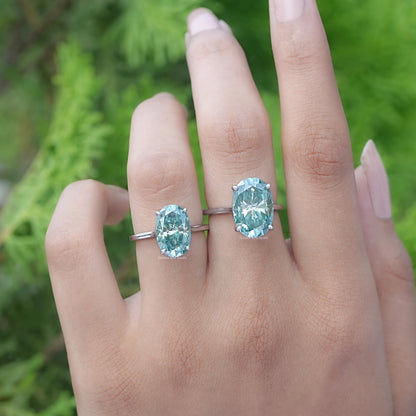 Front View of A Blue Green Oval Moissanite Solitaire Ring in two fingers
