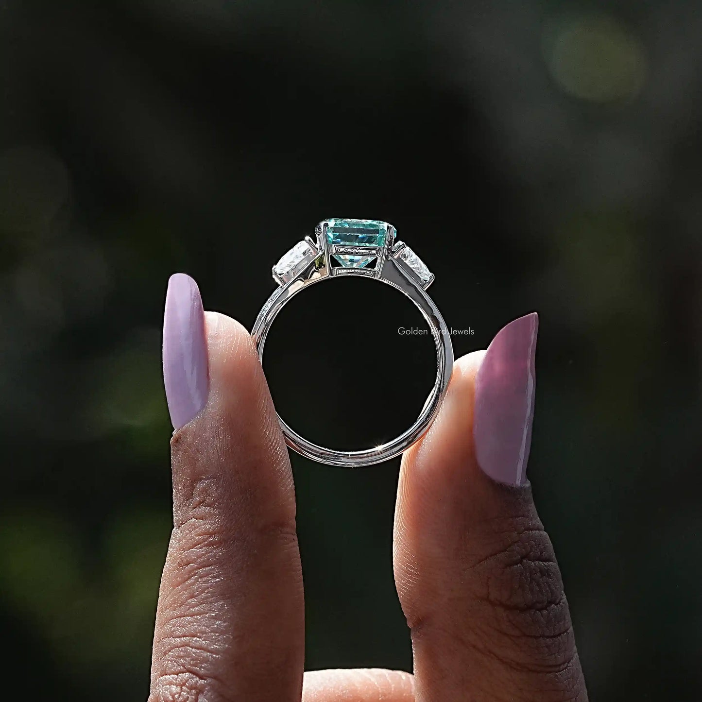Back View of Blue Radiant Cut Moissanite Three Stone Ring In two fingers
