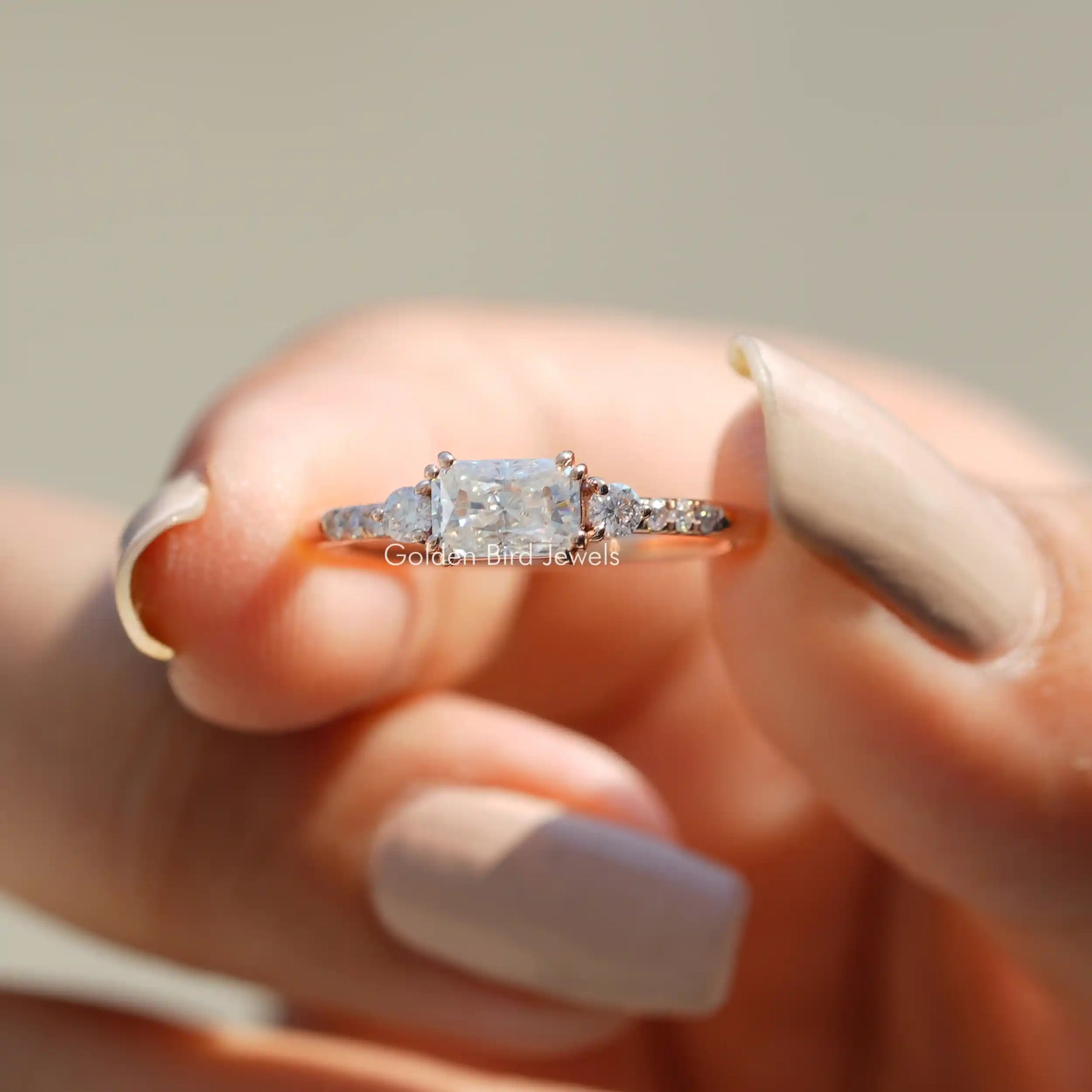 Two fingers holding the East West Radiant Cut Moissanite Engagement Ring