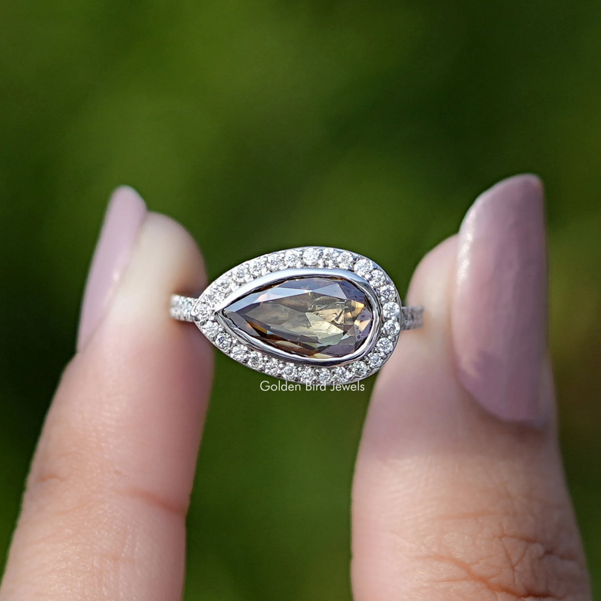 Two fingers holding the Rose Cut Pear Moissanite Halo Ring