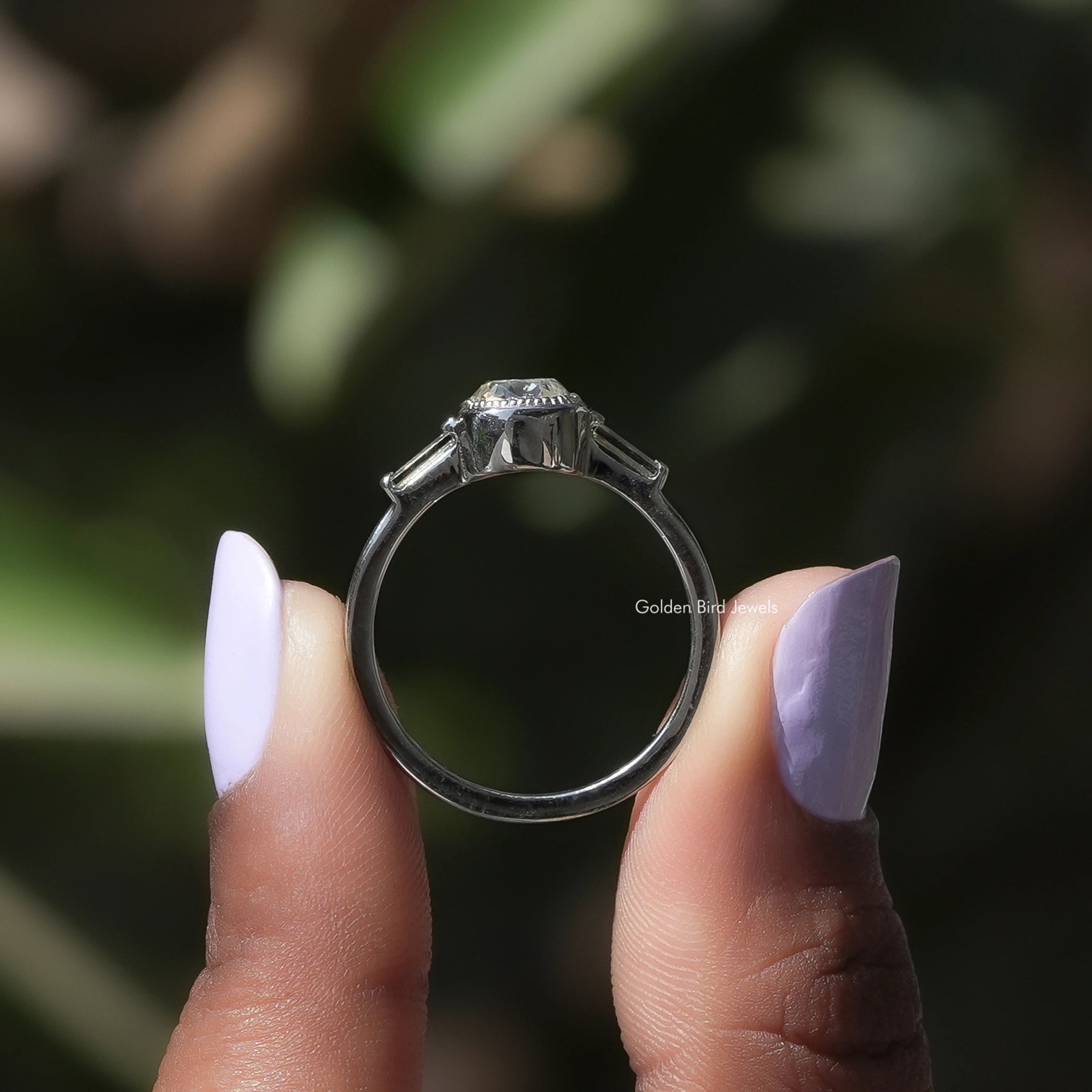 Back View of A Cushion Cut Three Stone White Gold Ring In two fingers