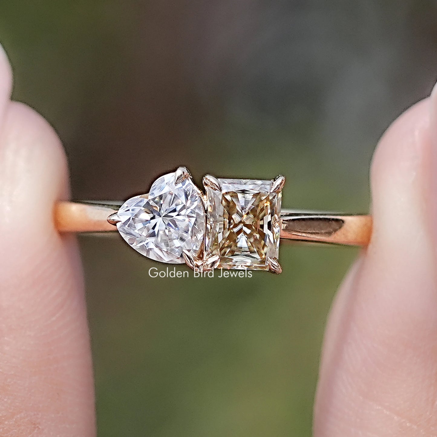 Front view of Radiant And Heart Cut Moissanite Two Stone Ring in two fingers 
