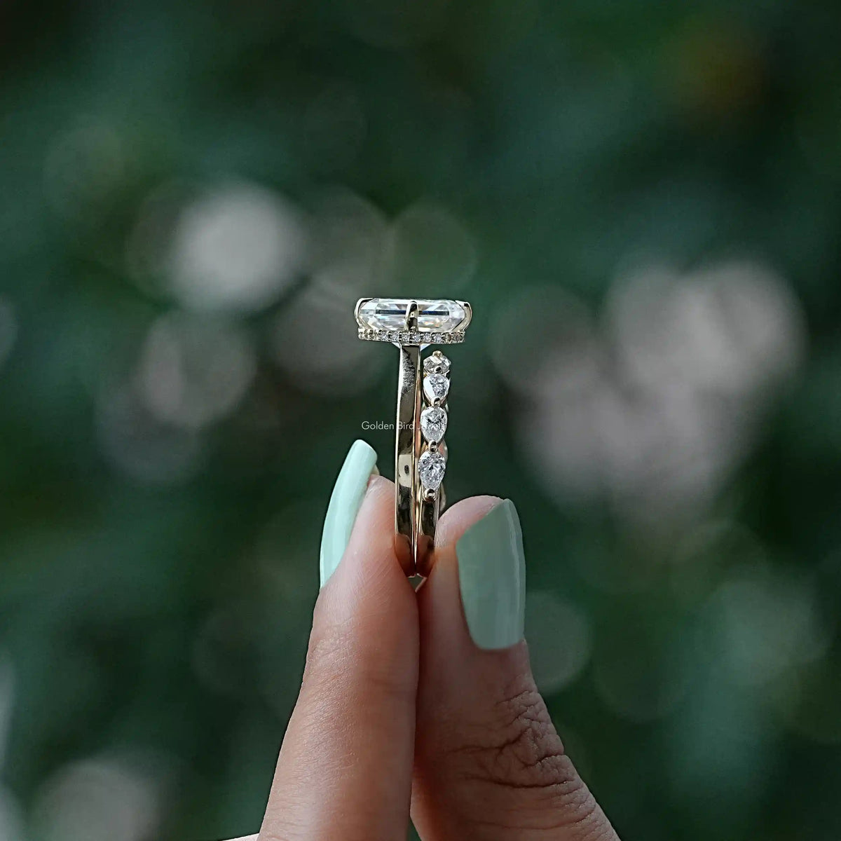 Side View of A Moissanite Radiant And Pear Cut Ring Set In two fingers