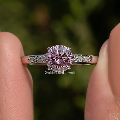 Pink gemstone ring held between two fingers with a blurred green background